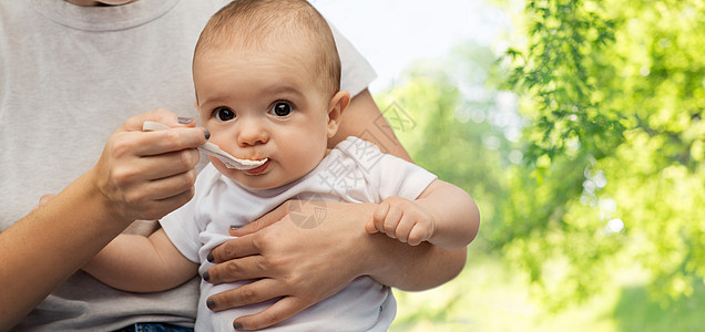 孩子,饮食食物的母亲用勺子喂养小婴儿绿色的自然背景用勺子喂小宝宝来亲近妈妈图片