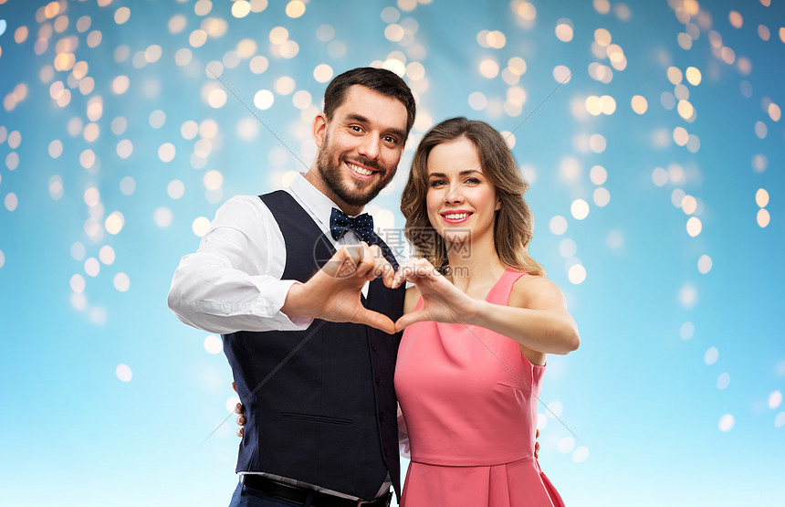 情人节,爱人的幸福的夫妇穿着派服装,蓝色背景的节日灯上做手势快乐的夫妇情人节做手心图片