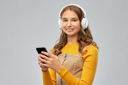 音频设备技术人员的微笑的十几岁女孩耳机听音乐智能手机灰色背景戴耳机听音乐的十几岁女孩图片