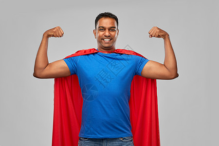 超级力量人的印度男子红色超级英雄斗篷他的肌肉灰色背景穿着超级英雄斗篷的印度男人展示了他的力量图片