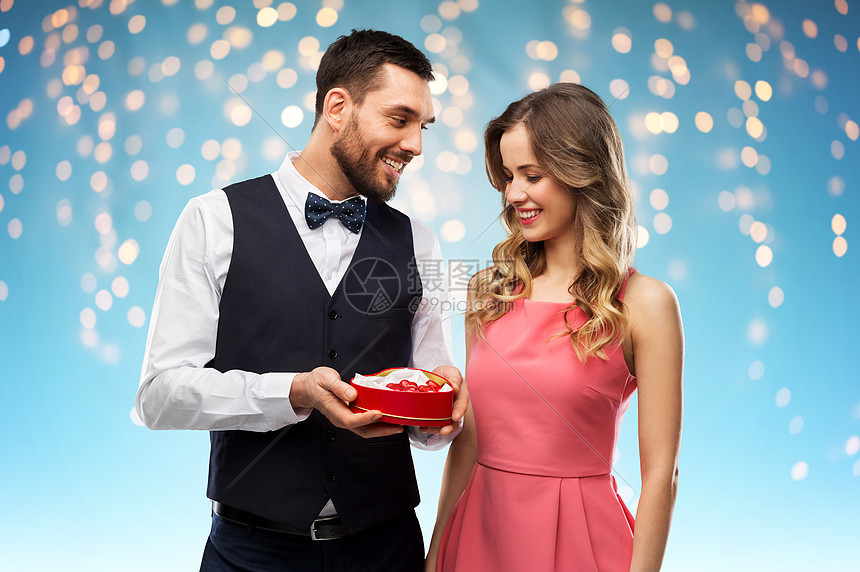 情人节人们的幸福的夫妇与巧克力盒的形状,假日灯的蓝色背景幸福的夫妇与巧克力盒的形状的心图片