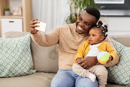 家庭,父亲人的快乐的非裔美国父亲与小女儿家里用智能手机自拍快乐的父亲婴儿家里自拍图片