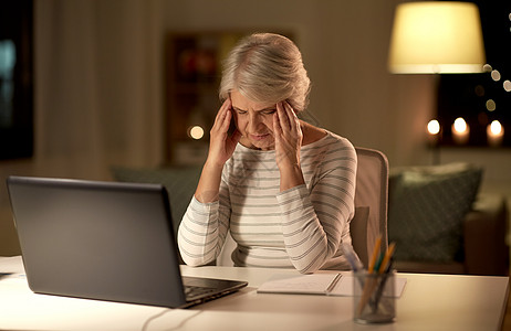 技术,老年压力疲惫或压力大的老年妇女,有笔记本电脑,晚上家头痛疲惫的高级女人晚上家带笔记本电脑背景图片