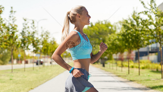 运动,健康的生活方式人们的微笑的年轻妇女与健身跟踪器沿着道路城市街道背景微笑的年轻女人户外跑步图片