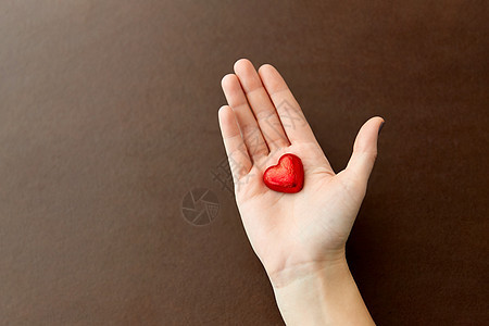 糖果,糖果食品手心形巧克力糖果红色箔纸包装棕色背景手红色心形巧克力糖图片