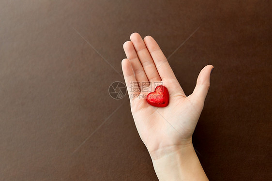 糖果,糖果食品手心形巧克力糖果红色箔纸包装棕色背景手红色心形巧克力糖图片