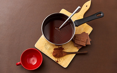 糖果,糖果烹饪锅与融化的热巧克力,可可粉勺子,红色陶瓷杯木板棕色背景锅里有热巧克力杯子可可粉图片