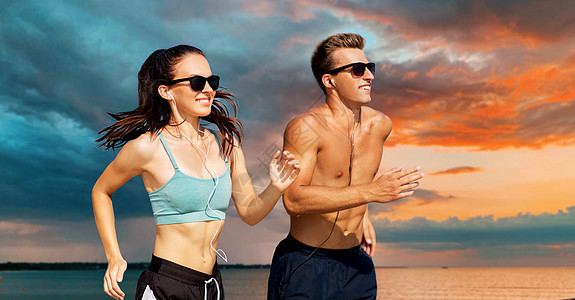 健身,运动技术快乐的夫妇与耳机运行海上日落天空的背景夫妇带着耳机海滩上跑来跑去图片