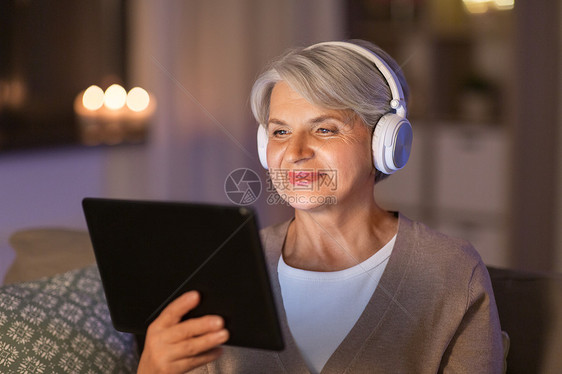 技术,人生活方式的快乐的高级妇女耳机平板电脑电脑家里听音乐晚上戴耳机听音乐的高级女人图片