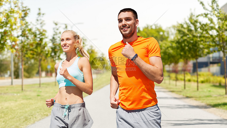 运动,健康的生活方式人们的微笑夫妇与健身跟踪者沿着道路城市街道背景快乐的夫妇与健身跟踪器户外运行图片