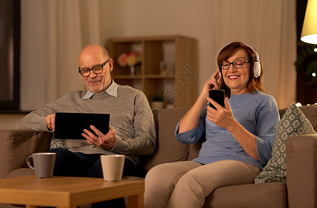 互联网背景技术,老年人人的快乐的老年夫妇与平板电脑,耳机智能手机家里晚上幸福的老年夫妇家带背景