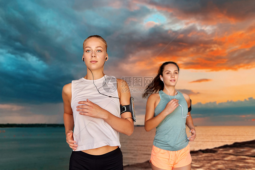健身,运动健康的生活方式年轻的妇女或女朋友戴着带智能手机的,背景上跑过大海日落的天空带着耳机智能手机的年图片