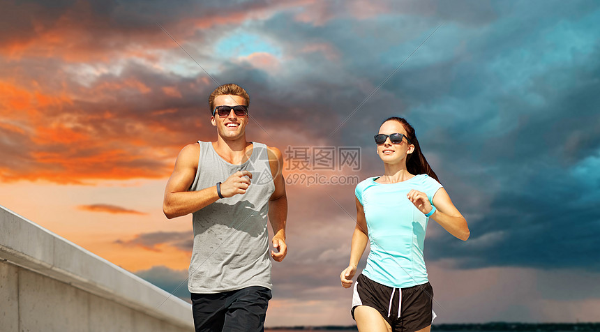 健身,运动健康的生活方式幸福的夫妇穿着运动服装太阳镜跑日落的天空背景穿着运动服的夫妇户外跑步图片