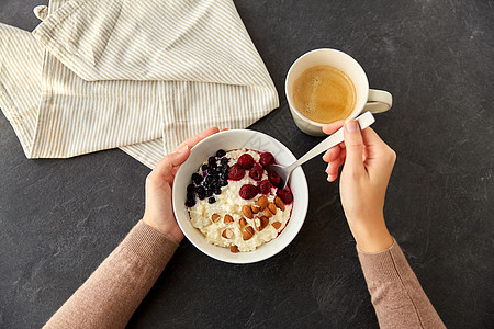 食物早餐女人的手与勺子吃粥碗与野生浆果,杏仁坚果咖啡石板石桌手粥早餐杯咖啡背景图片