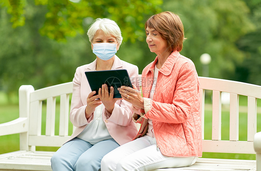 健康安全大流行两名高级妇女或朋友戴着医用口罩,以防止病平板电脑电脑坐夏季公园的长凳上老年妇女戴着医用口罩,公图片