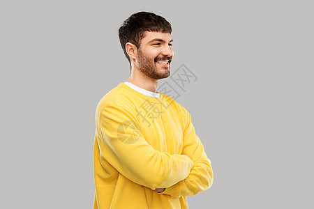 人们的快乐的微笑年轻人穿着黄色运动衫,双臂交叉灰色背景上穿着黄色运动衫的年轻人交叉手臂图片