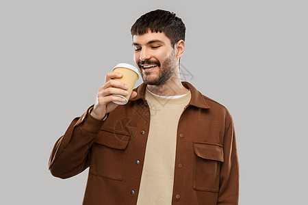 饮料人们的微笑的年轻人喝咖啡外卖杯灰色背景快乐的年轻人外卖杯里喝咖啡图片