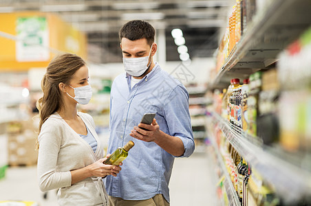 食物购物,消费主义大流行幸福的夫妇戴着口罩,以防止病疾病,智能手机购买橄榄油杂货店或超市夫妇戴着口罩,带着电话图片