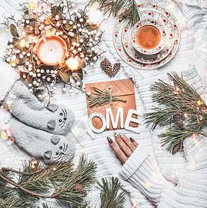 舒适的冬季圣诞节回家心情平躺的生活方式与女的手针织毛衣,有趣的温暖的小猫袜子,冷杉树枝,燃烧的蜡烛,波基,杯茶文字回图片