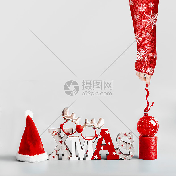 女手穿着红色毛衣,白色雪花,着圣诞球的丝带圣诞背景与圣诞老人小屋,单词圣诞节,蜡烛红色假日球站浅灰色背景现代的图片