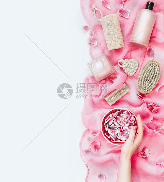 女手水碗,粉红色毛巾上有鲜花,有各种环保的护肤美容工具白色背景上的刷子海绵浮石化妆品上面的风景平躺图片