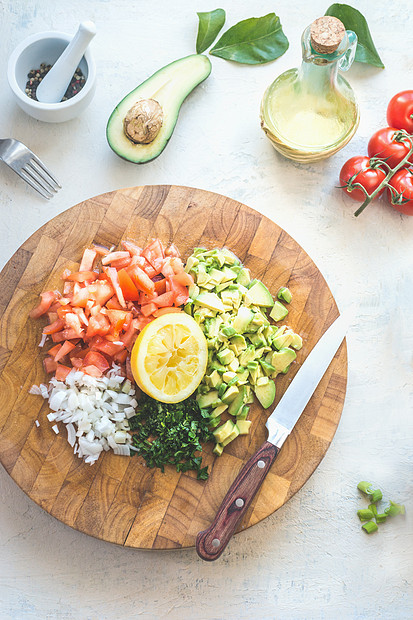 准备美味的新鲜鳄梨番茄沙拉白色厨房桌子背景,顶部视图木制切割板上切碎的蔬菜健康的食物素食午餐或小吃图片