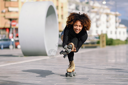 年轻合身的黑人妇女溜冰鞋骑户外的城市街道上阳光明媚的日子里,微笑的女孩留着AFRO的发型骑着溜冰鞋的黑人女人城市街图片