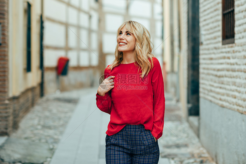 快乐的年轻金发女人走街上微笑的金发女孩,穿着红色衬衫站户外快乐的年轻金发女人走街上图片