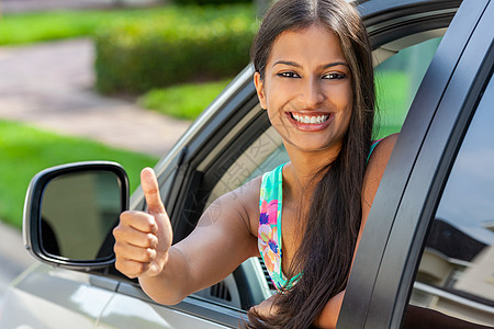 美丽的印度亚洲年轻妇女或女孩车里站出来,夏天的阳光下竖起大拇指,微笑着,牙齿完美,头发长发租车,驾驶考试的图片