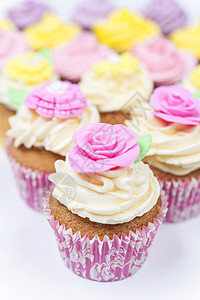 杯子蛋糕与糖霜或霜,粉红色,紫色,黄色奶油与绿叶,玫瑰花卉装饰拍摄白色背景图片