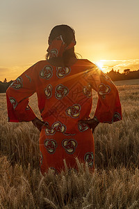 非洲妇女穿着传统的衣服,站着,看着,双手放臀部,日落或日出时,大麦或小麦作物的地里图片