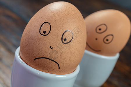 情感两个煮鸡蛋白蛋杯与绘制快乐悲伤的脸木桌上图片