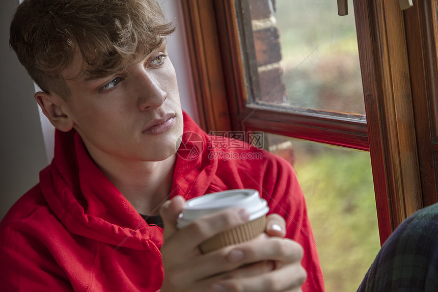 悲伤沮丧体贴的青少年男孩男青少年年轻人看着窗外喝咖啡或茶图片