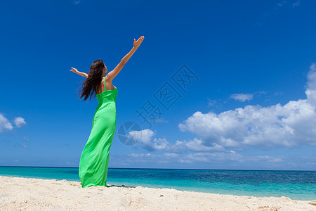 穿着绿色连衣裙的女人热带海滩上摆姿势,举起手臂海滩上穿裙子的女人图片