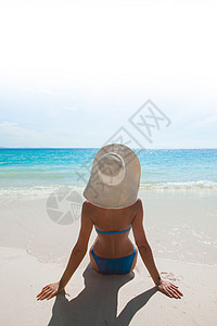 海洋落日穿着比基尼太阳帽的女人坐海滩上看着大海海边的太阳帽里的女人背景