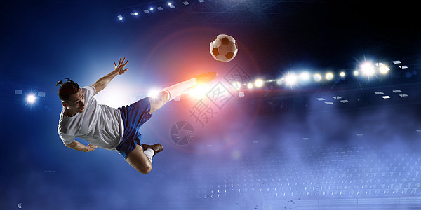 足球运动员夜间体育场用燃烧的灯光踢个球体育场上的足球运动员跳起来踢球图片