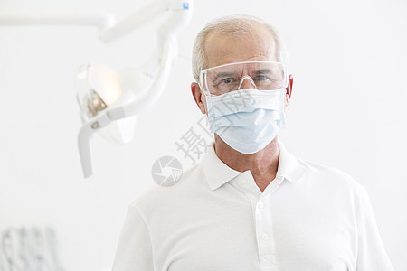 牙科诊所戴口罩眼镜的高级牙医肖像图片