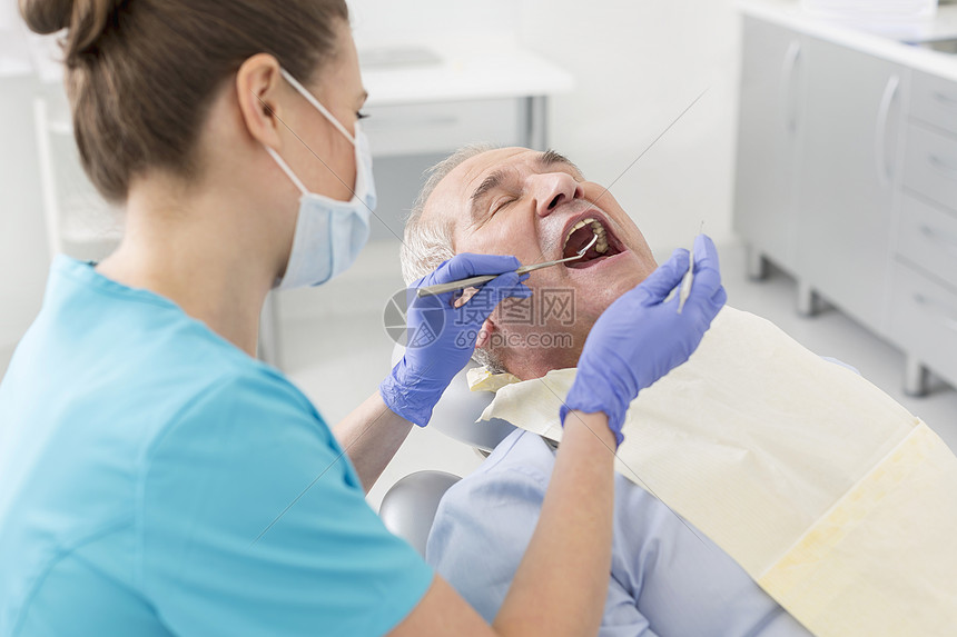 牙科医生治疗过程中用角度镜定标器检查老年患者的口腔图片
