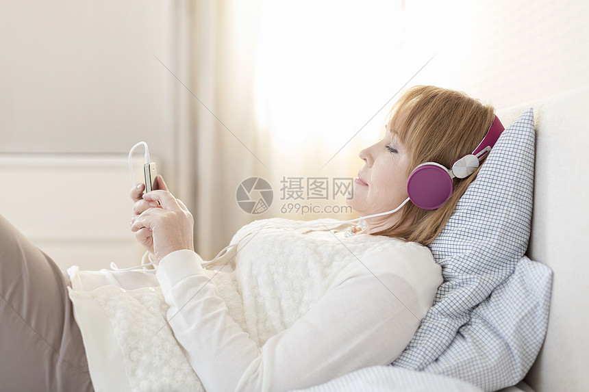 侧面看成熟的女人家里躺床上听音乐图片