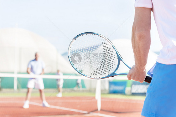 成年男子网球场上与朋友起玩球拍的中段图片