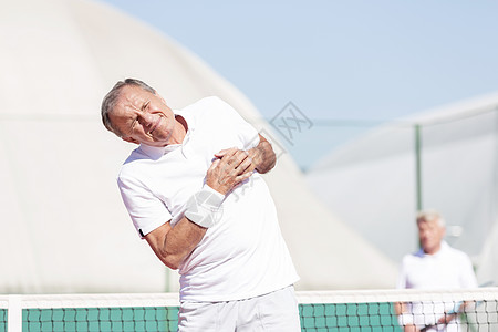 阳光明媚的日子里,网球比赛中,老人站朋友面前做胸痛的鬼脸图片