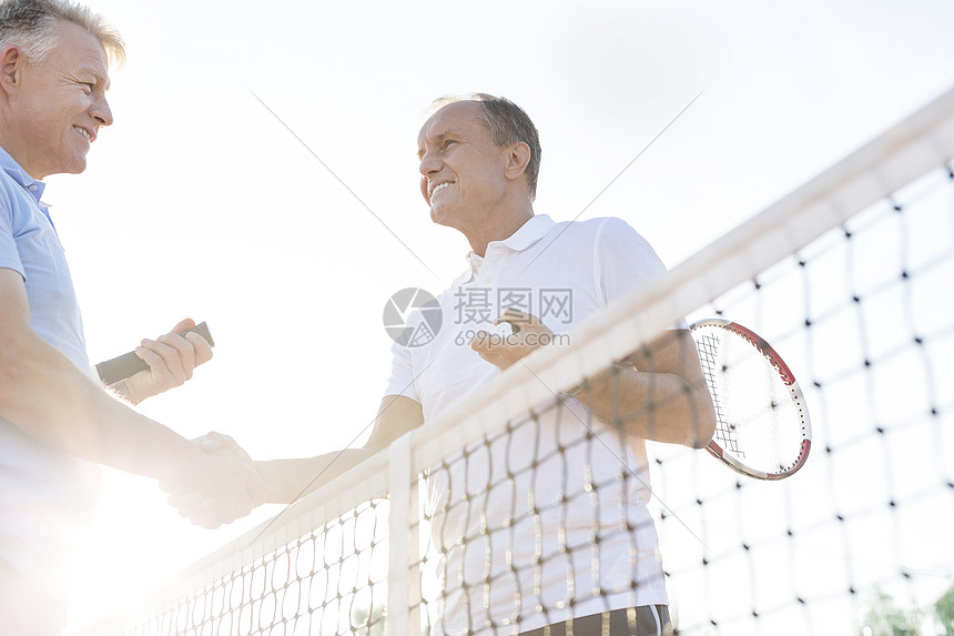 低角度的观点,微笑的男人握手,同时站网球场晴空图片