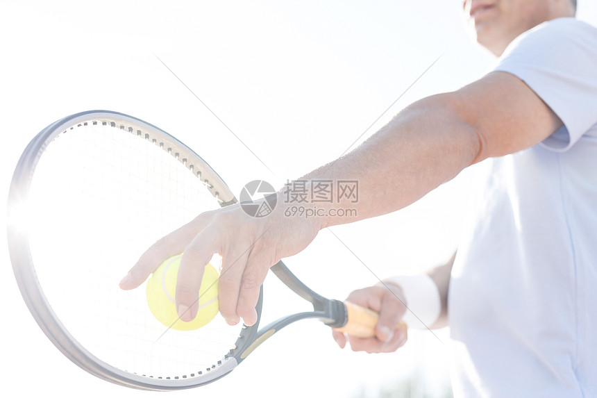 阳光明媚的日子里,成年男子晴朗的天空上打网球图片