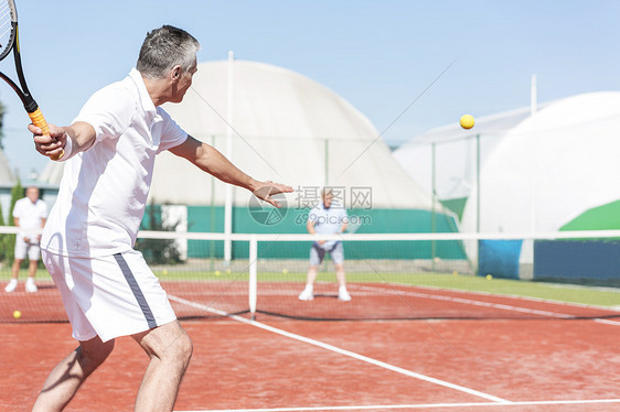 男子夏季周末红场打双打比赛时挥动网球拍图片