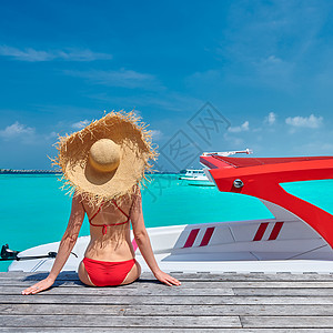 穿着红色比基尼的女人坐木船码头上马尔代夫的暑假背景图片