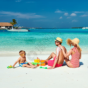 家庭游海滩上的家人,三岁男孩的轻夫妇女男背部涂防晒霜马尔代夫的暑假背景