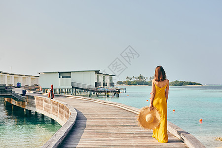 穿着连衣裙的女人走热带海滩的木板路上马尔代夫的暑假图片