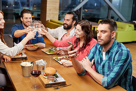 技术,生活方式人们的男人与朋友用餐智能手机餐厅的信息餐厅智能手机上的男士短信图片