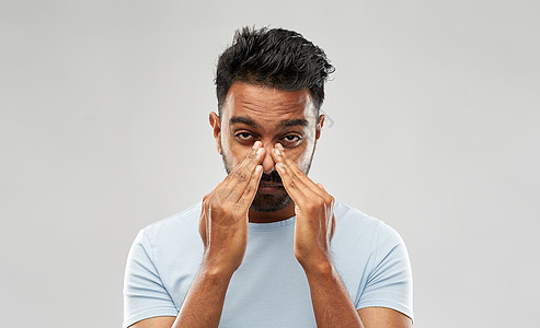 健康问题人们的印度男人灰色背景上摩擦鼻子印度男人揉鼻子图片