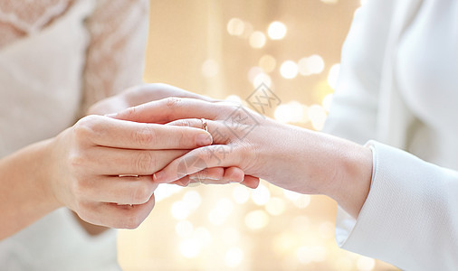 ,同婚姻LGBT亲密的女夫妇的手戴上结婚戒指节日的灯光背景用结婚戒指把女夫妇的手闭上图片